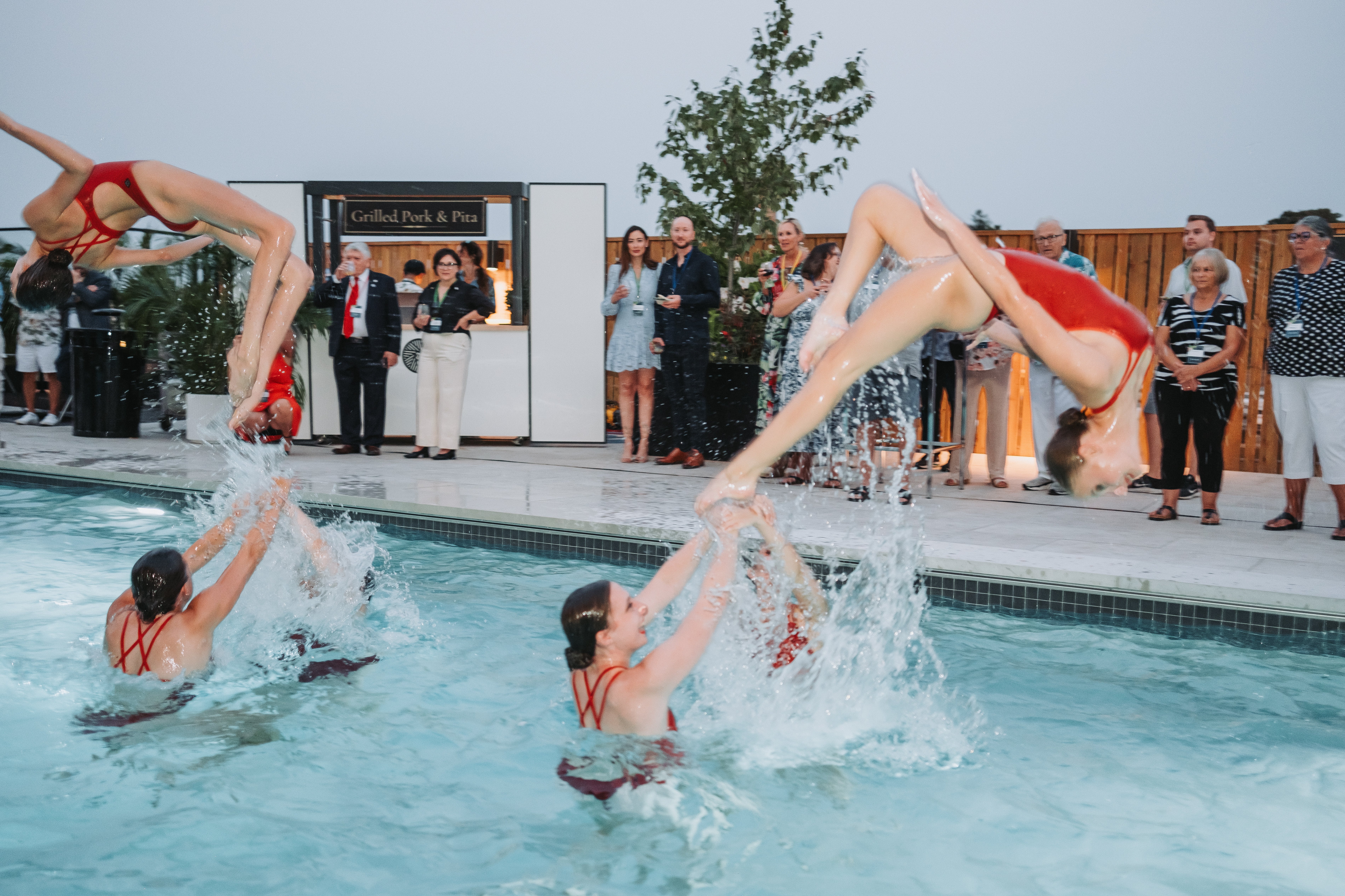 AquaMermaid synchronized swimming team performing at an upscale corporate event, well-dressed audience watching